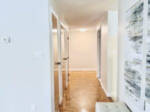 Interior Furnished Model Unit Hallway, wood floors, neutral toned walls, abstract art on walls. 4 doors in hallway.