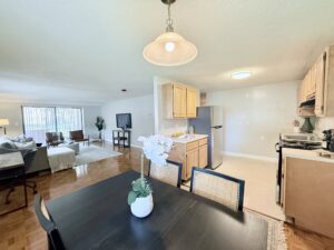 Interior Furnished Kitchen and Dining Area, attached to living room, wood floors, table in dining room, laminate floors in kitchen, light brown wood cabinetry, stainless steel appliances.