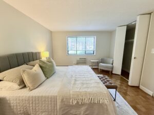 Interior Furnished Unit Bedroom, Wood floors, Neutral toned walls, folding closet doors, window on farside wall.