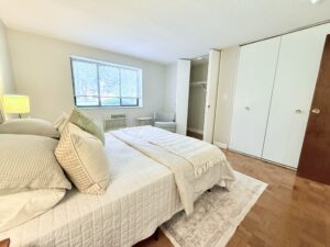 Interior Furnished Unit Bedroom, Wood floors, Neutral toned walls, folding closet doors, window on farside wall.