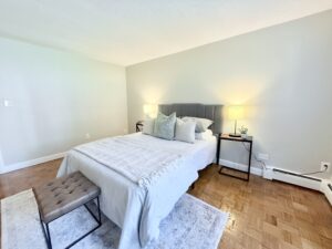 Interior Furnished Living Room, King Size Bed, Two nightstands, bench at the end of the bed, wood floors, neutral toned walls.